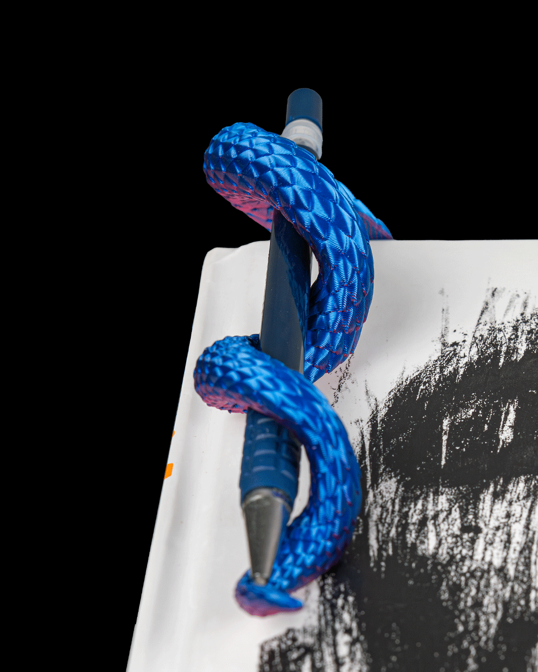 Close up of Dragon Tail pen holder wrapping around a pen on the edge of a notebook