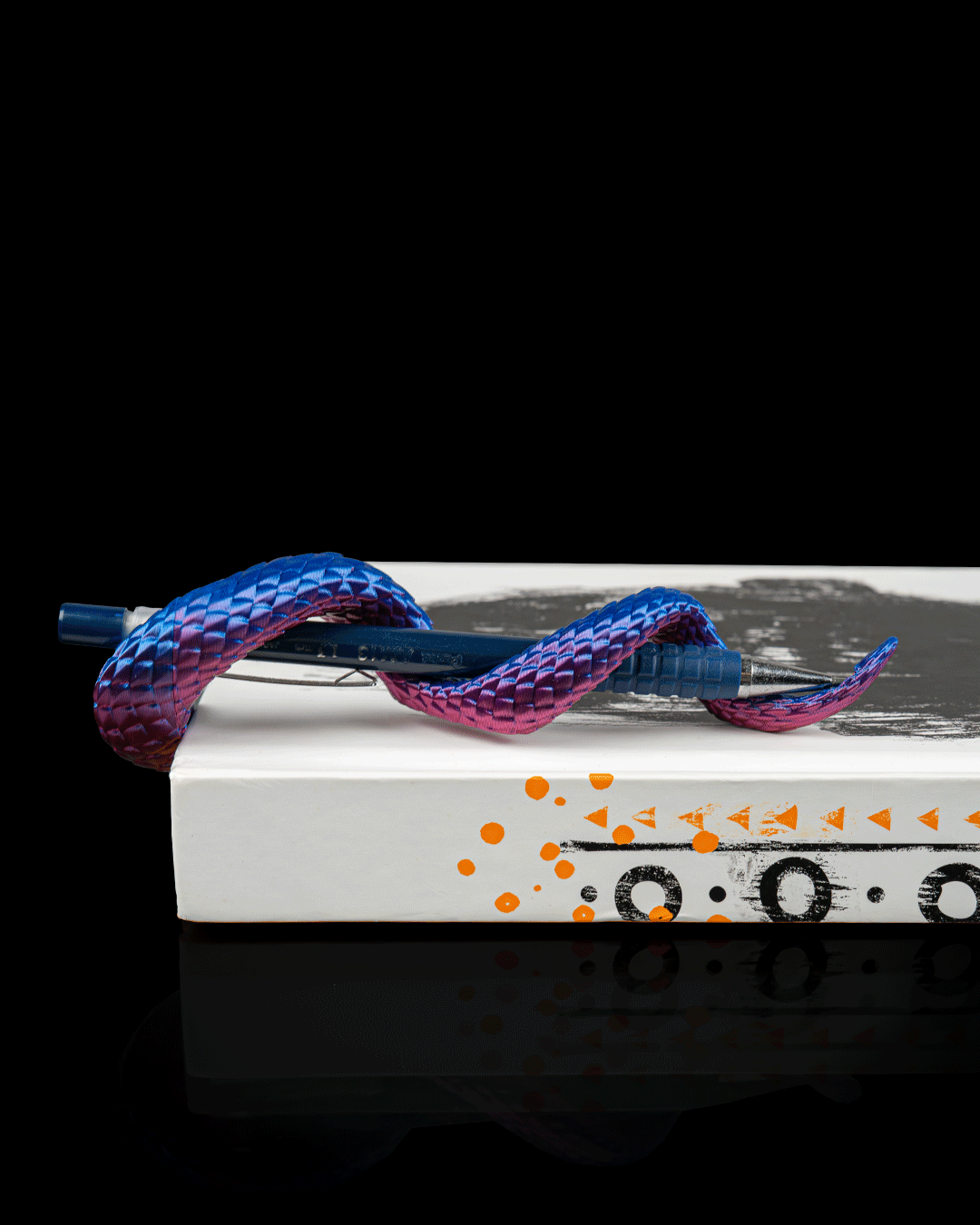 Dragon Tail pen holder side view on notebook with blue and pink dual color finish holding a pen